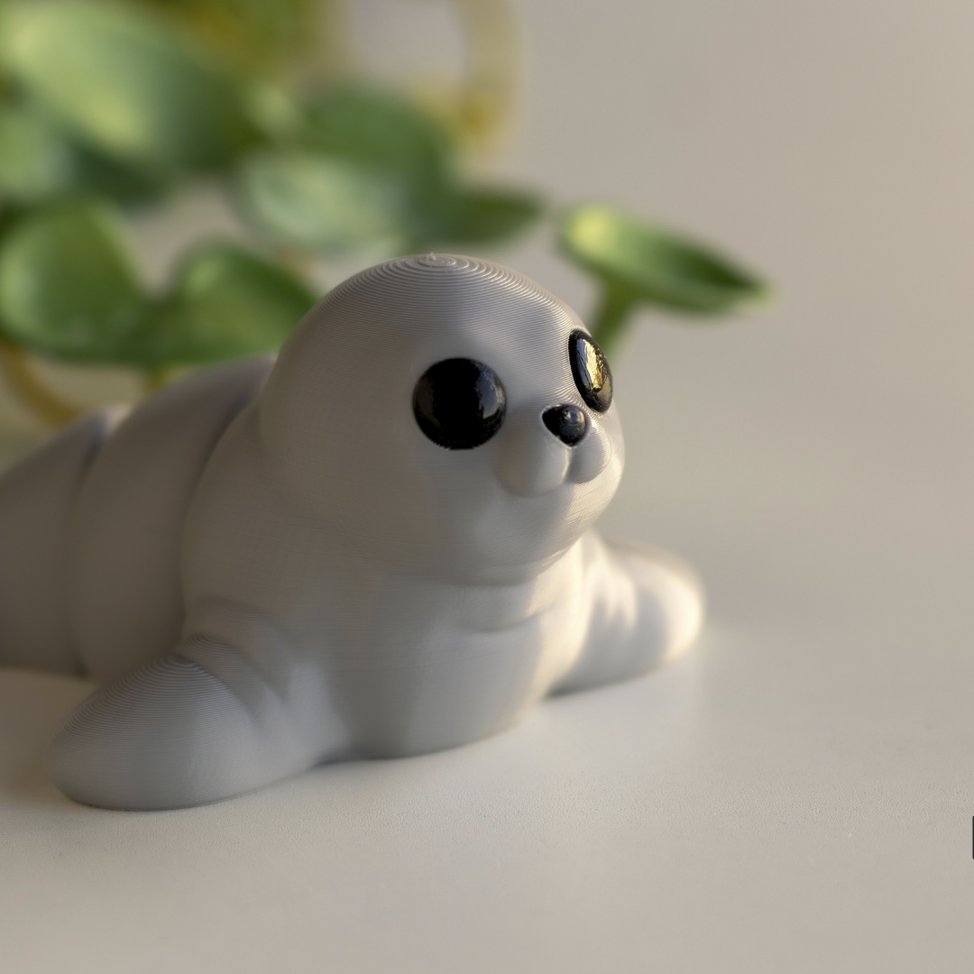 A close-up of a small, white, cartoon-like seal figurine with large black eyes and a small nose, sitting on a white surface.