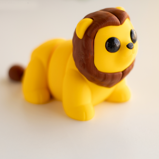 A yellow toy lion with a brown mane and eyes is sitting on a white surface.